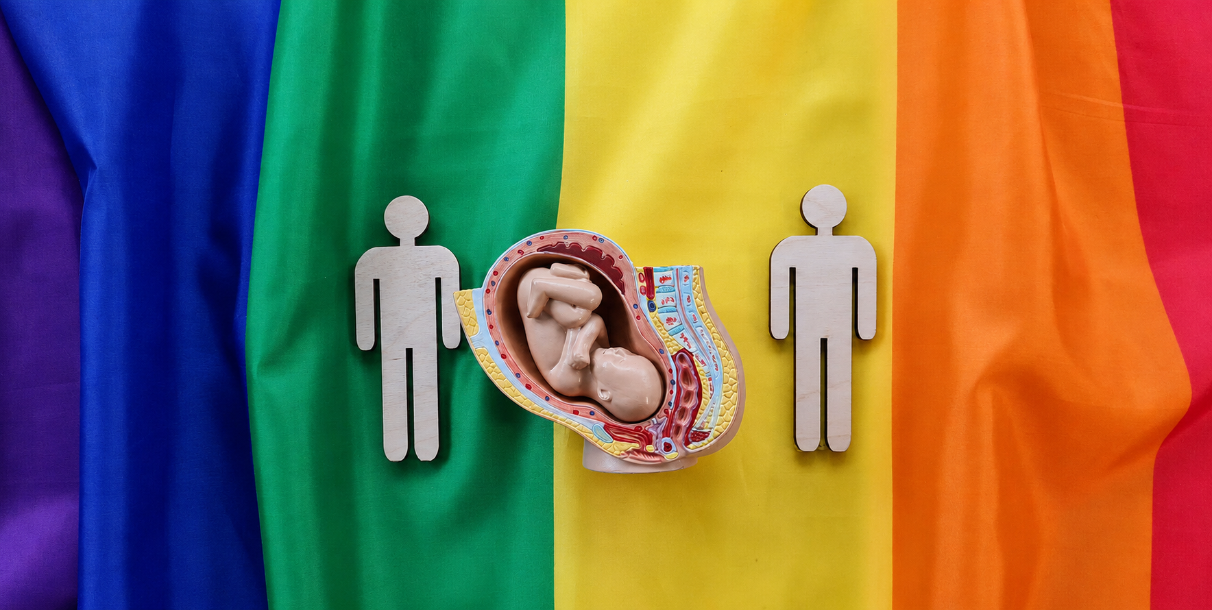 彩虹旗上的准父母木制人偶与妊娠模型,象征 LGBTQ+ 家庭通过代孕成家
